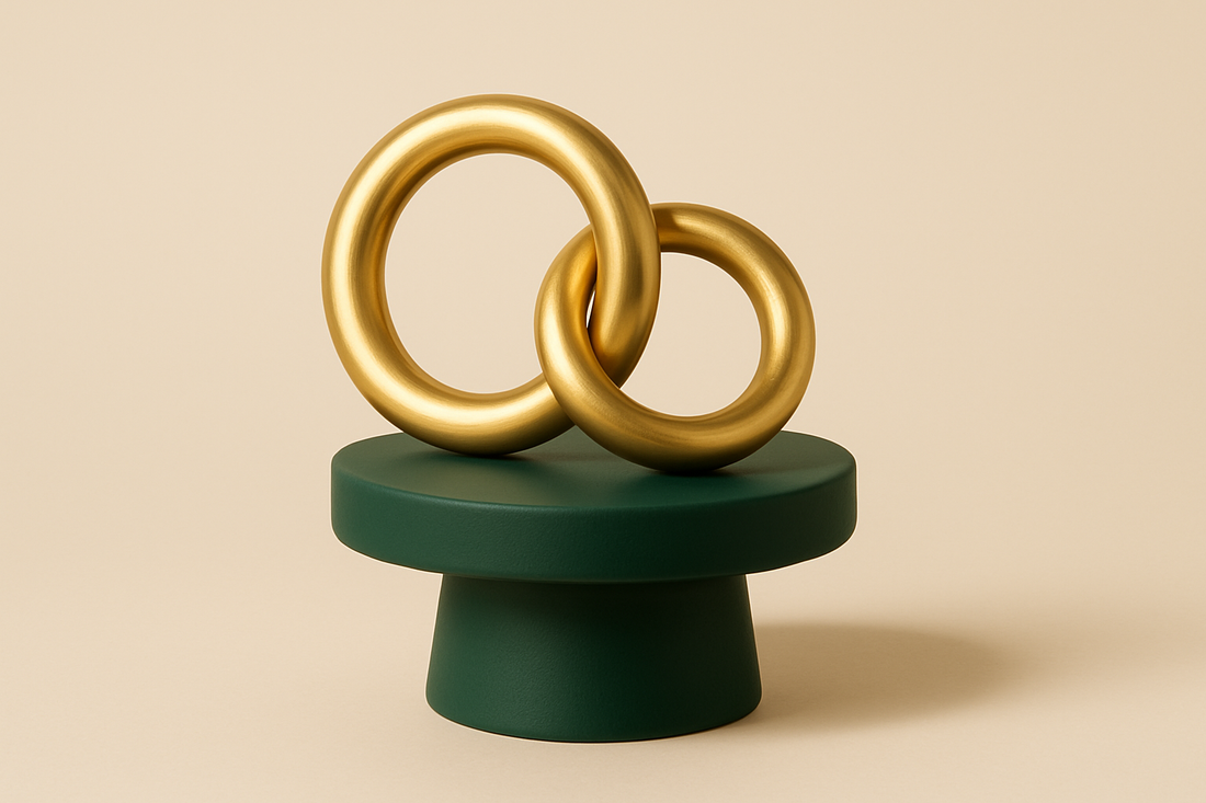 Dois anéis de latão polido entrelaçados como elos de corrente sobre um pedestal cerâmico verde-escuro, ao fundo bege suave, sob iluminação clara de estúdio com sombras suaves.